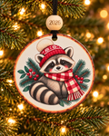 Raccoon Christmas ornament with raccoon in red knit hat and buffalo plaid scarf among pine boughs, 4 inch round wood Christmas ornament with 2026 bead by Bandit Laser
