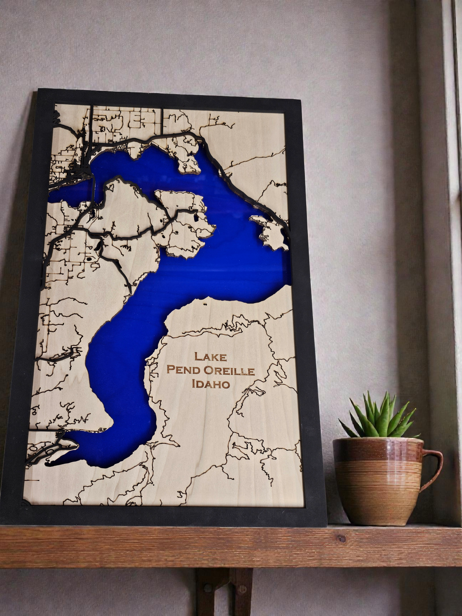Wooden map of Lake Pend Oreille Idaho with blue water feature, framed on a shelf.