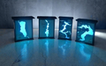Four glowing blue light boxes with abstract designs on a reflective surface.