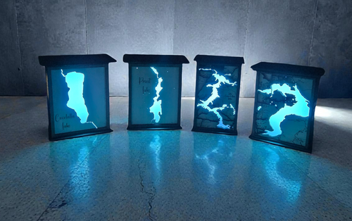 Four glowing blue light boxes with abstract designs on a reflective surface.
