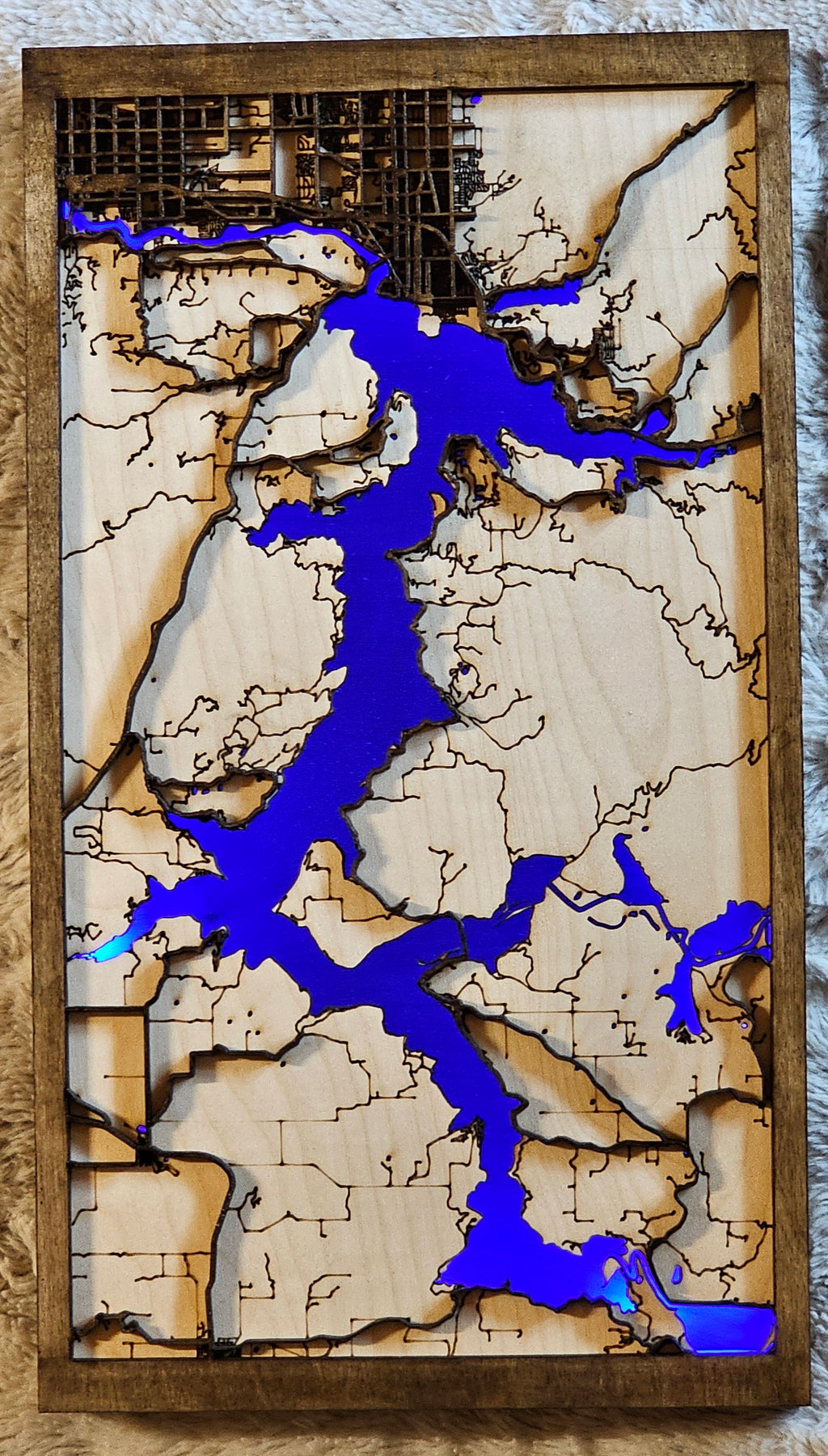 Wooden wall art with a map design featuring blue waterways on a textured surface.