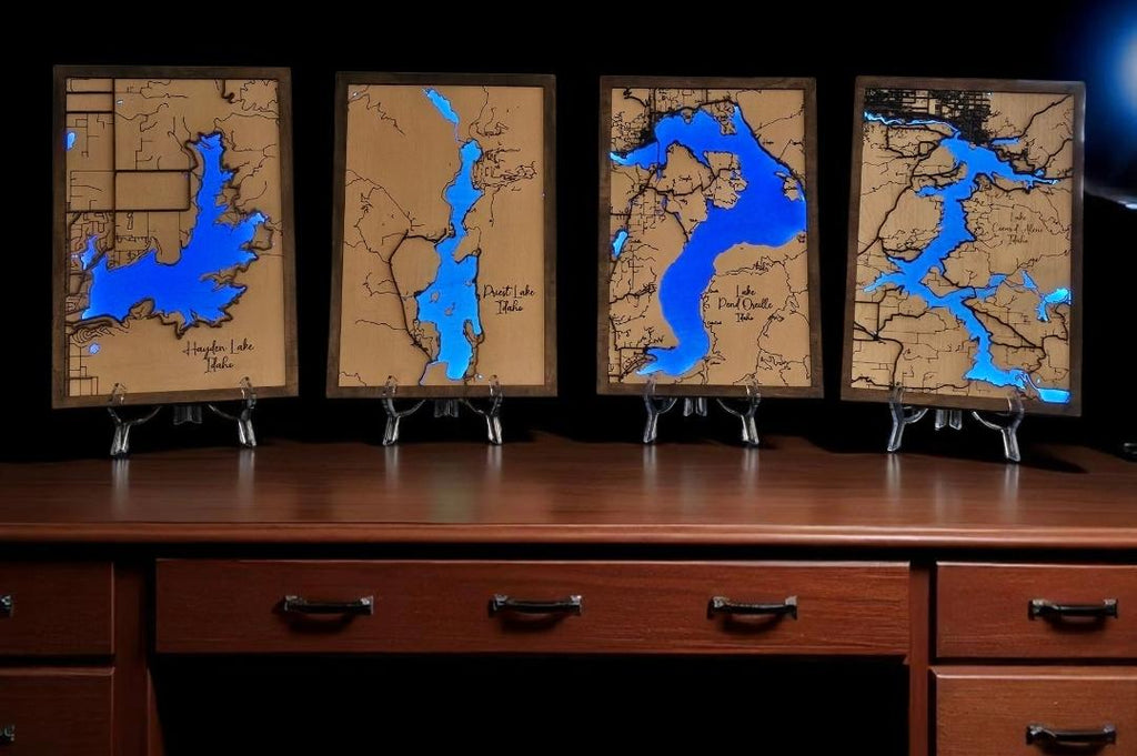 Four framed maps with blue water features displayed on a wooden surface.
