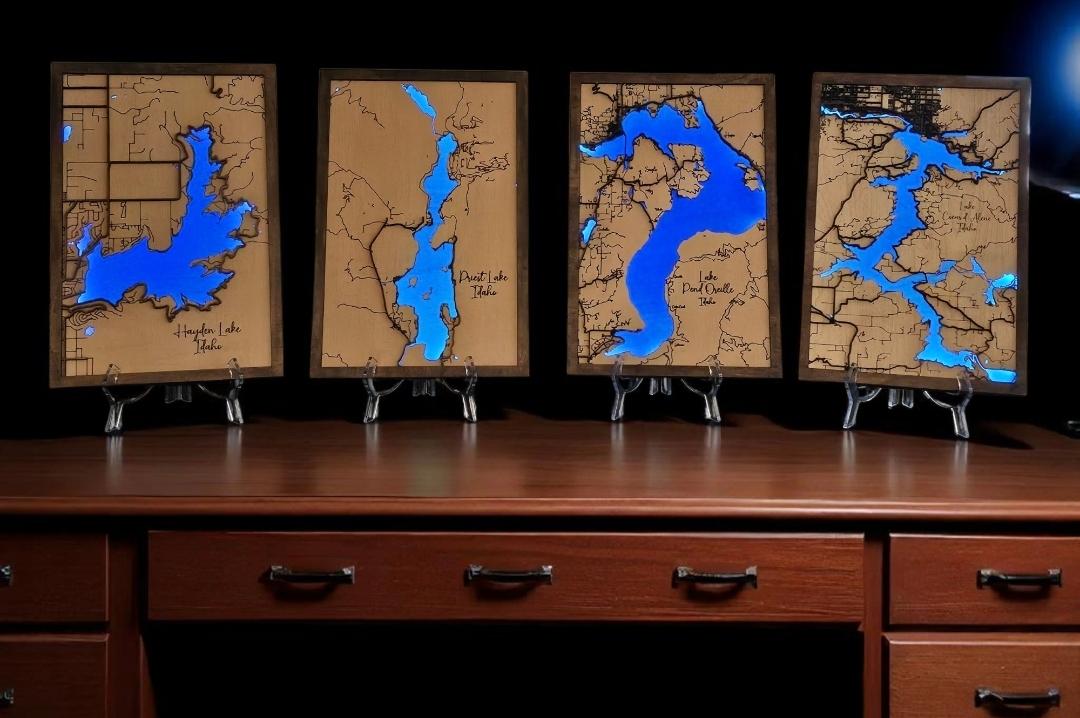 Four framed maps with blue water features displayed on a wooden surface.