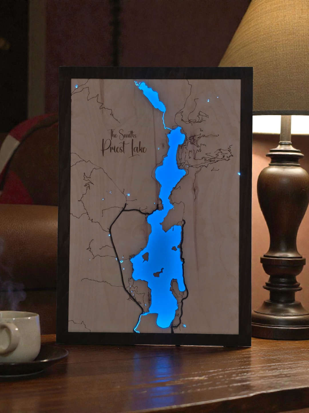 Map of Priest Lake with a blue light on a wooden surface next to a cup and lamp.