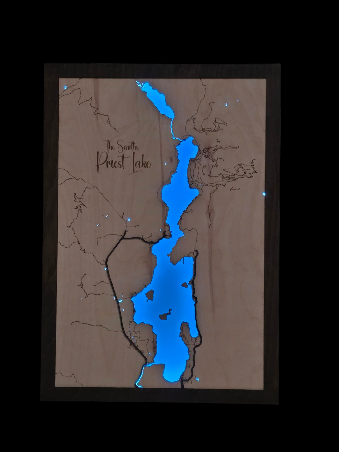 Wooden map of Priest Lake with blue water and brown land, framed.