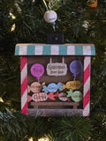Decorative Christmas ornament with names on a candy shop sign against a Christmas tree background.