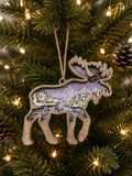 Layered wood moose ornament with purple mountain scene, deer, and pine trees, hanging on a Christmas tree